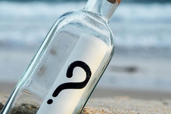 Bottle with question mark on the label in the sand at the beach