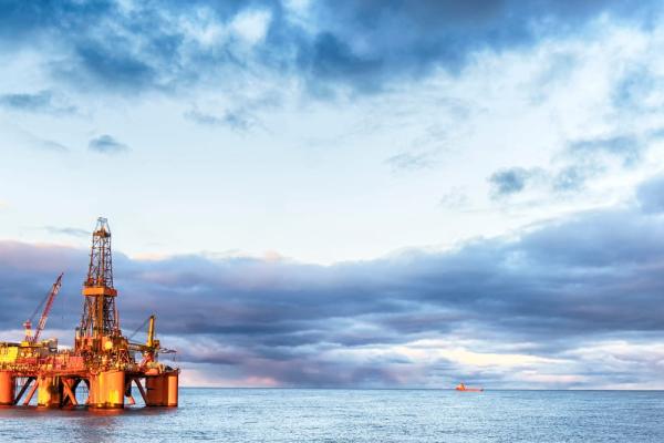 A brightly lit oil rig with a single, huge, derrick float in the cold looking waters with a tiny tanker ship in the horizon.