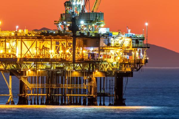 Offshore oil platform off the coast of California against a moody, orange sky as the sun sets behind the rig.