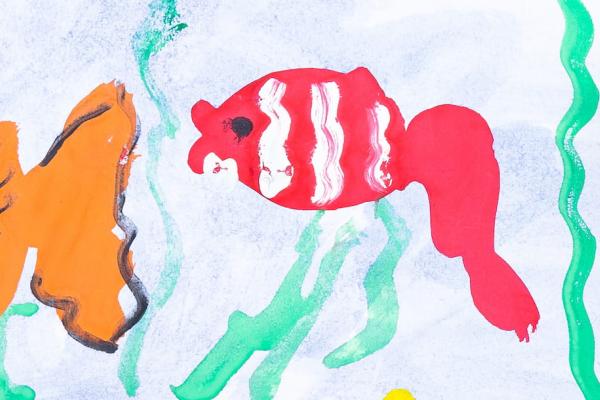 Top view of child hands with markers painting picture of fish on paper.