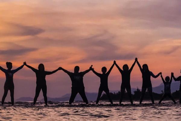 Silhouettes of 21 people standing in ankle deep water, holding hands like paper dolls