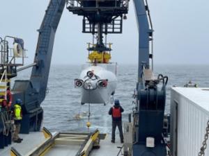 Alvin submarine being launched from a crane off the back of a ship at sea