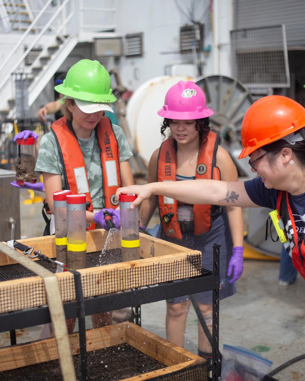 Three researchers wearing safety gear prepare seafloor sediment samples for analyses. 
