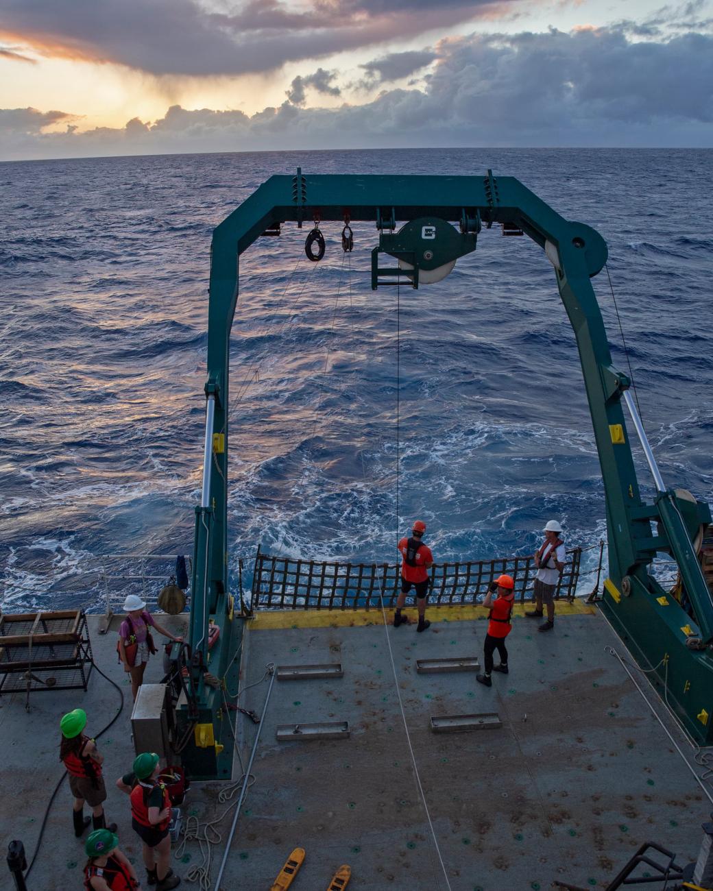 Researchers on the deck of the Kilo Moana research vessel at sea during sunset.