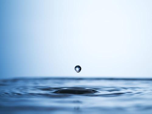 Studio shot of a water droplet falling into a puddle of water.