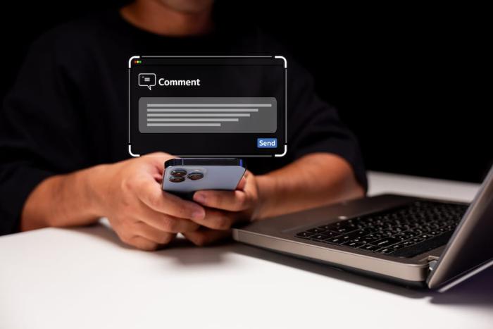 A pair of human hands working a cell phone in front an open laptop