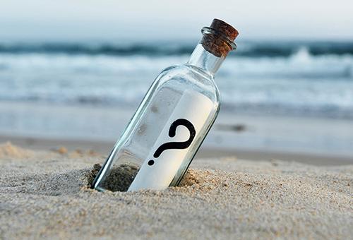 glass bottle with a question mark on the label in the sand by the beach