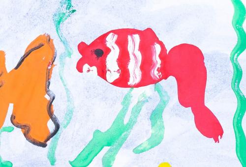 Top view of child hands with markers painting picture of fish on paper.